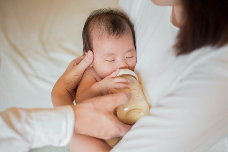 newborn baby held by parent bottle feeding